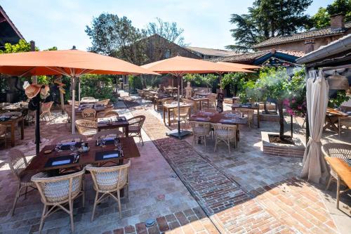 een patio met tafels, stoelen en parasols bij Hôtel Le Résinier in Le Barp