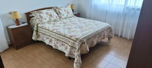 1 dormitorio con 1 cama con manta de flores y mesita de noche en Camiño Loureiro, en Combarro