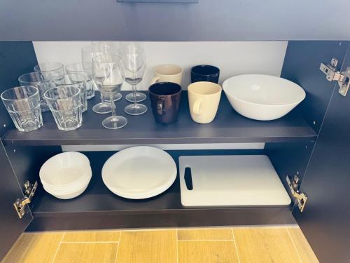 a shelf with plates and cups and wine glasses at Alto Turtas Apartamentai in Šiauliai
