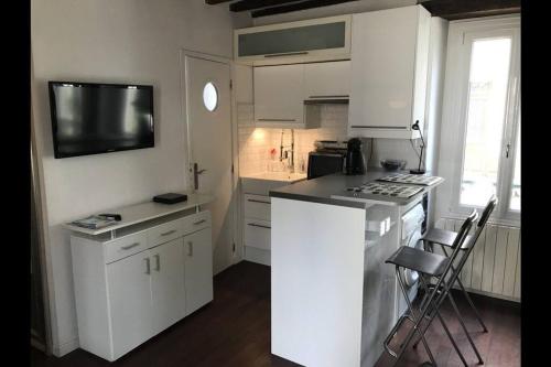 a kitchen with white cabinets and a tv on the wall at Charmant studio plein centre in Fontainebleau