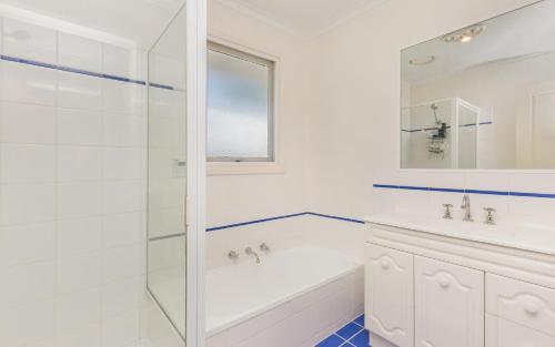 Clouston Cottage في Heathcote: حمام أبيض مع دش وحوض استحمام ومغسلة