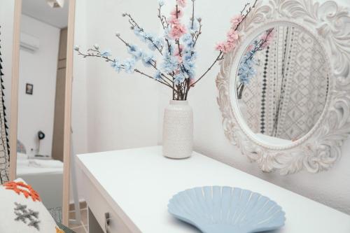 Villager's Art Apartment في باراديسيون: طاولة بيضاء مع مزهرية عليها زهور بجوار مرآة