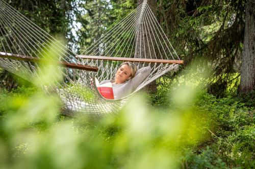 a woman laying in a hammock in a forest at Hotel Neuhaus in Saalbach Hinterglemm
