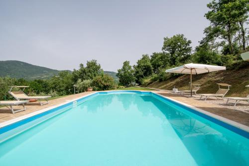 a blue swimming pool with chairs and an umbrella at Villa in esclusiva - Pugnano Alto in Lisciano Niccone