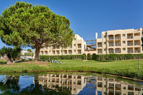 a building with a tree next to a body of water at The Navigator - Palm Oasis Alvor - All Inclusive in Alvor