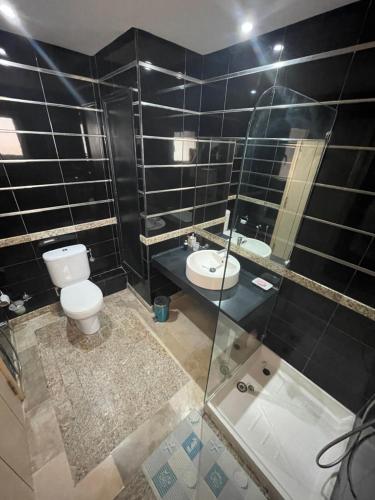 Baño de azulejos negros con aseo y lavamanos en Beachfront Apartment 105- Hotel Andalucia, en Bizerte