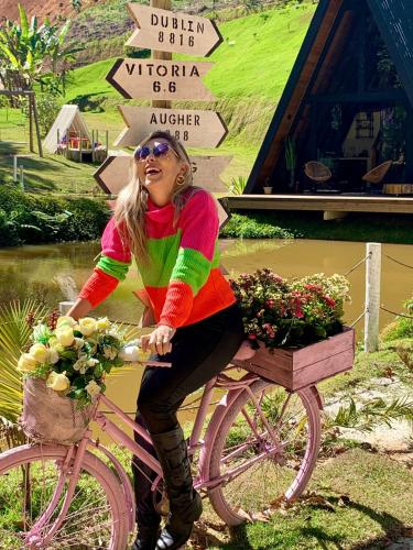 a woman sitting on a pink bike with flowers at Cabana A frame Paraíso nas Montanhas in Marechal Floriano