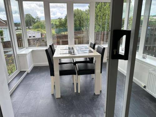 ein weißer Tisch und Stühle in einem Raum mit Fenstern in der Unterkunft Family friendly detached 2 bed home, Loch Lomond in Bonhill