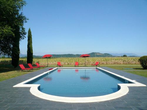 a swimming pool with red chairs and umbrellas at Agriturismo Beria de Carvalho de Puppi in San Giovanni al Natisone