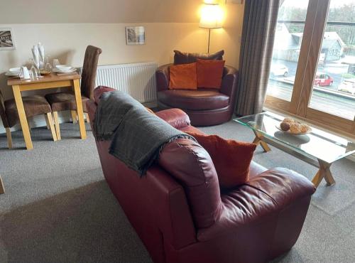 a living room with a brown leather couch and a table at Balmaha Lodges and Apartments in Balmaha