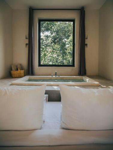 a bathroom with a tub with a window and pillows at Yum Kaax Boutique Villa in Tulum