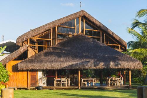 a building with a straw roof and tables and chairs at Hotel Villa Balidendê in Barra Grande