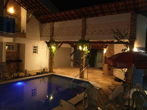 a swimming pool at night with chairs and an umbrella at Flat Villagio Coqueiro in Luis Correia