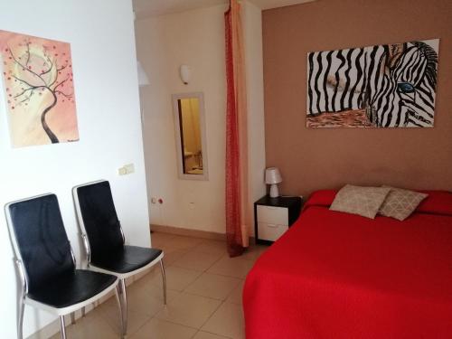 a bedroom with a red bed and two black chairs at Apartamentos Vista Bahia in Los Cristianos