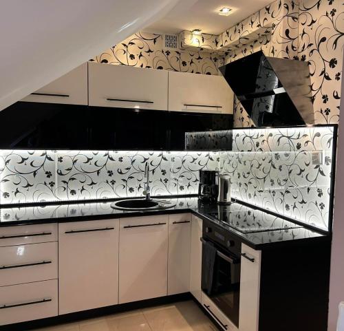 a kitchen with white cabinets and black and white wallpaper at Apartament Mazurska Natura in Szczytno