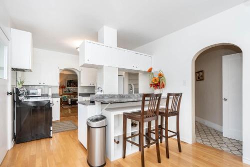 uma cozinha com armários brancos e um bar com duas cadeiras em River view house em Winnipeg