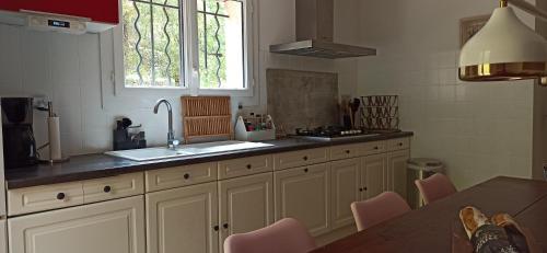 une cuisine avec des armoires blanches, un évier et une fenêtre dans l'établissement Villa au cœur de la Provence, à Lorgues