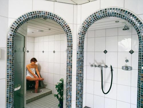 two archways in a bathroom with a woman sitting in the shower at Heidehotel Hildfeld in Winterberg