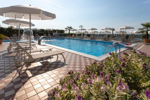 una piscina con panchine e ombrelloni in un resort di Hotel Mirafiori a Lido di Jesolo