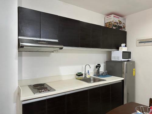 eine Küche mit schwarzen Schränken, einer Spüle und einem Kühlschrank in der Unterkunft Uptown CDO Staycation in Cagayan de Oro