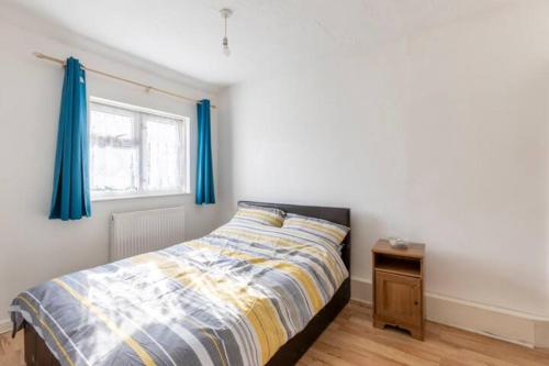 a bedroom with a bed with blue curtains and a table at cosy 1 bedroom flat near Barking town centre in Barking