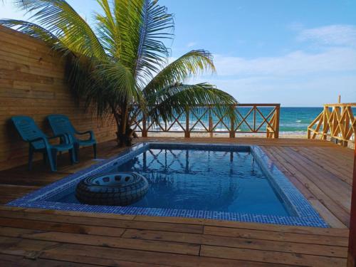 a swimming pool with a tire and two chairs and the ocean at Villa Devonia - Beachfront Cabins with Pool at Tela, HN in Tela