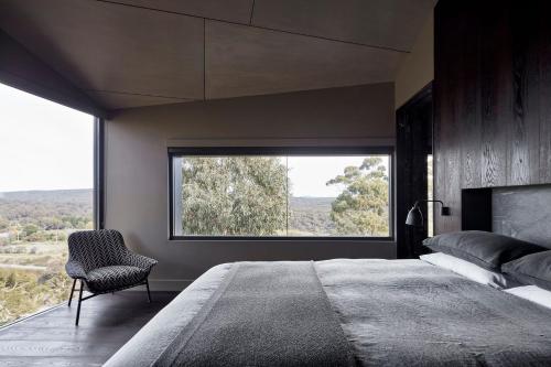 a bedroom with a large window and a bed and a chair at Breakneck Gorge Oikos in Hepburn Springs