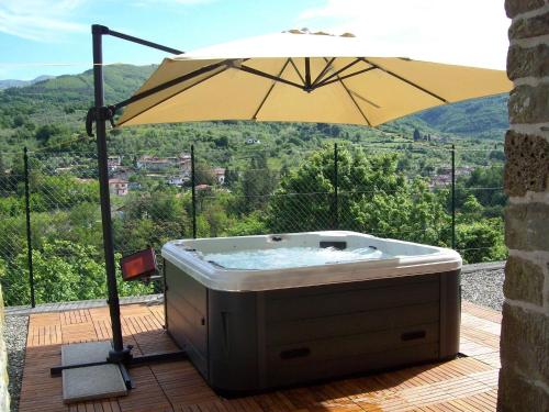 uma banheira de hidromassagem com um guarda-sol num deque em Flat with heated hot tub and shared pool em Casola in Lunigiana
