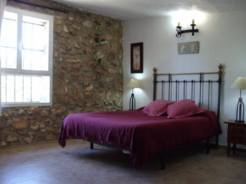 a bedroom with a bed with purple sheets and a stone wall at House No 02 median in Humilladero