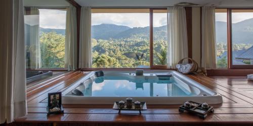 a large bath tub in a room with large windows at Mirante da Colyna Hotel & SPA in Monte Verde