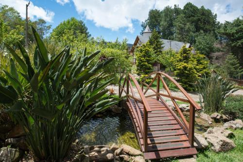a wooden bridge over a pond in a garden at Mirante da Colyna Hotel & SPA in Monte Verde
