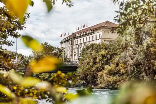 a building with flags on top of it next to a river at Hotel Weitzer Graz - Centre of Graz in Graz