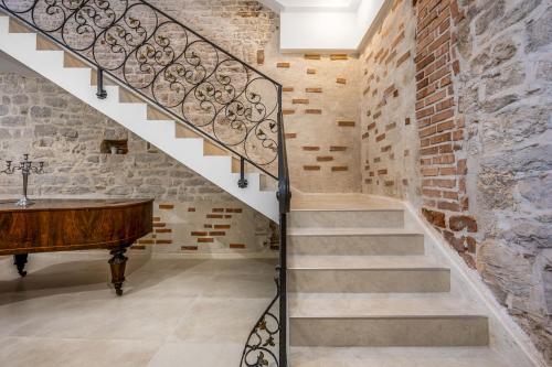 a staircase in a room with a piano and a brick wall at Sizgoric Palace Suites Sibenik in Šibenik