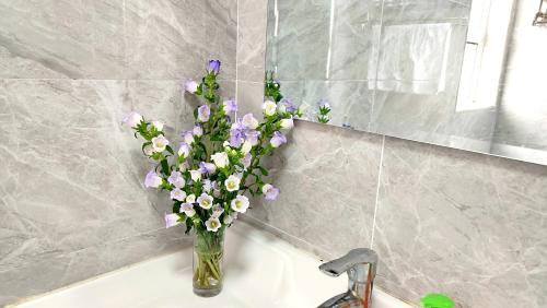 un jarrón lleno de flores púrpuras y blancas sentado en un fregadero en Jenny's Apartment, en Shanghái