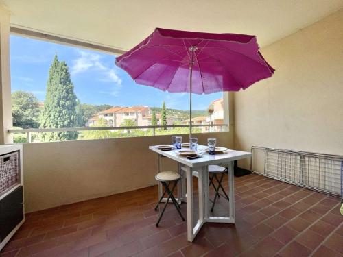 une table avec un parapluie violet devant une fenêtre dans l'établissement Appartement T2 avec piscine, 4 couchages - La Croix-Valmer - FR-1-226B-161, à La Croix-Valmer