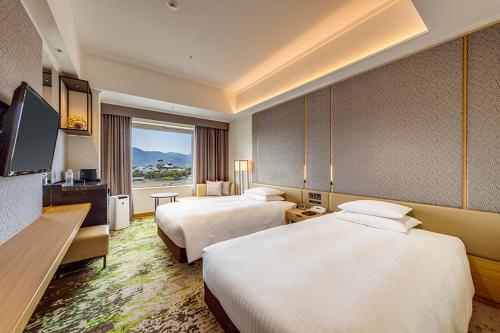 a hotel room with two beds and a flat screen tv at Hotel Nikko Kumamoto in Kumamoto