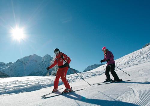 dos personas están esquiando por una pista cubierta de nieve en Alpenpension Elferblick, en Hirschegg