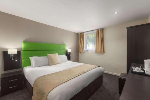 a bedroom with a large bed with a green headboard at Ramada Birmingham Oldbury M5 J2 in Oldbury