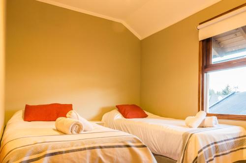 two beds in a room with yellow walls and a window at BOG Angostura Apartments in Villa La Angostura