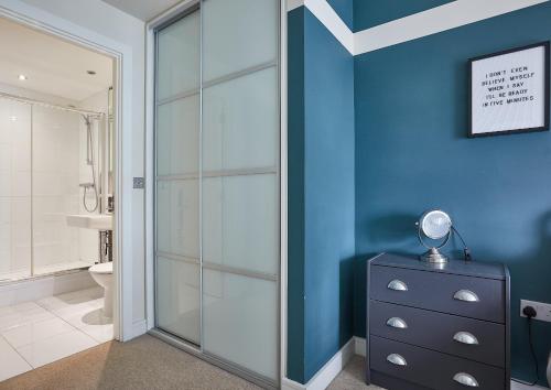a bathroom with a glass shower with a blue wall at The Glassworks by Ritual Stays in Hemel Hempstead