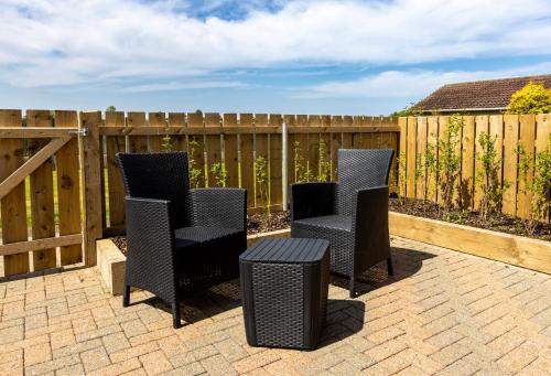a patio with three chairs and a table and a fence at Causeway Coast Retreats in Dervock