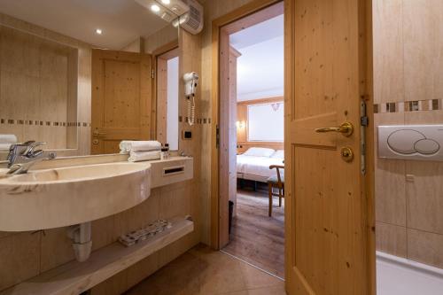 a bathroom with a sink and a mirror and a bed at Hotel Cristina in Pinzolo