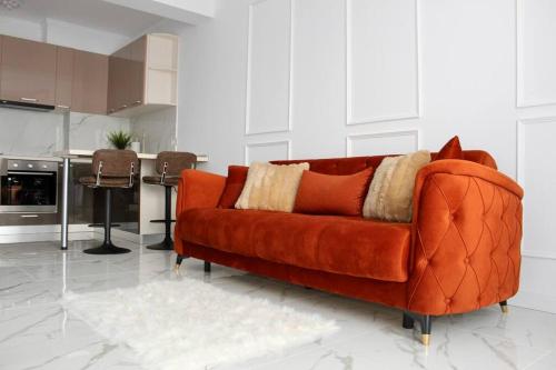 an orange couch in a living room with a kitchen at Luxe Central Apt: Free Parking in Oradea
