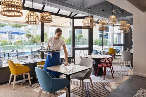 a woman standing in a restaurant with tables and chairs at Novotel Rennes Alma in Rennes