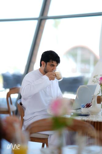 a man sitting at a table drinking a cup of coffee at Dibba Mountain Park Resort in Fujairah