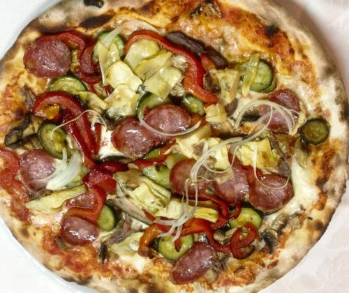 a pizza with pepperoni and vegetables on a plate at La Perla Hotel in SantʼAnna Arresi