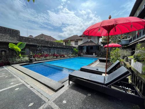a swimming pool with a red umbrella and a bench with at Kasapa Inn in Ubud