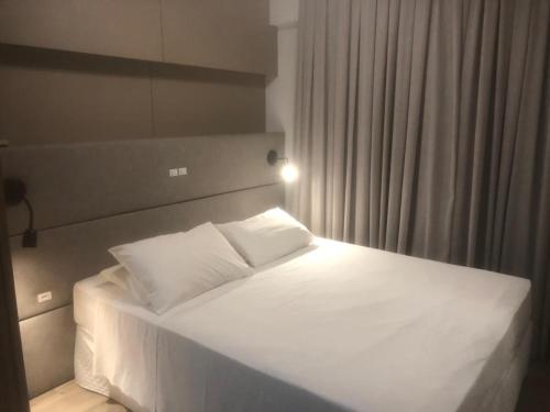 Una cama con sábanas blancas y almohadas en un dormitorio en Apart-hotel Central com Spa en Balneário Camboriú