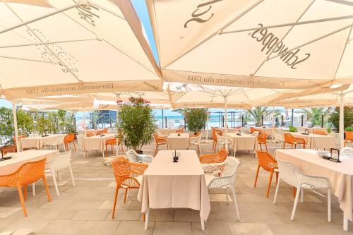 ein Restaurant mit weißen Tischen, Stühlen und Sonnenschirmen in der Unterkunft Hotel Malibu in Mamaia