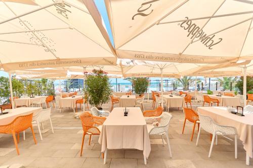 un restaurant avec des tables blanches, des chaises et des parasols dans l'établissement Hotel Malibu, à Mamaia